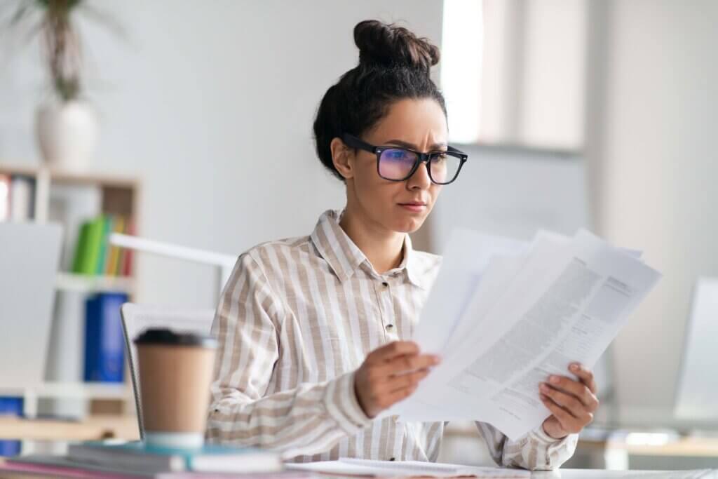 Paperwork concept. Focused female manager holding and reading paper or financial document, sitting at workplace Form 706-NA